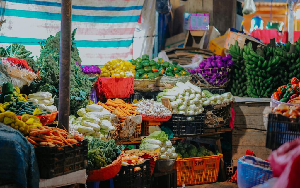 Vibrant assorted vegetables, including carrots, broccoli, green and peppers, and garlic are stacked on multi-colored crates in a market in Vietnam.